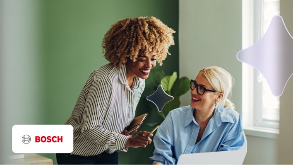 Duas mulheres à mesa sorrindo com uma parede verde ao fundo